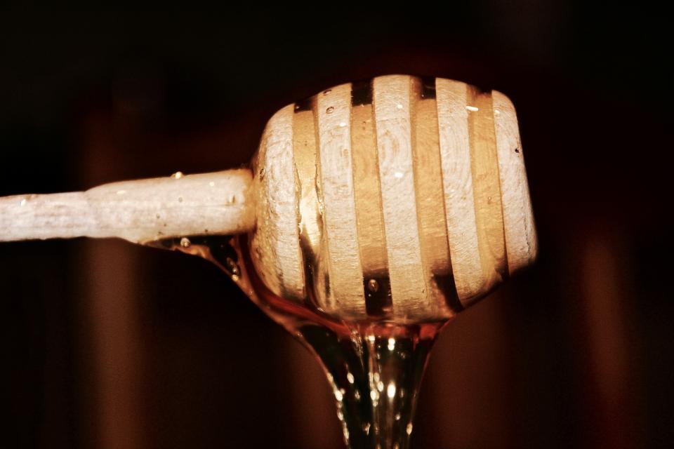 Golden raw honey dripping from a wooden honey dipper